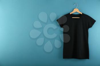 Hanger with blank black t-shirt on color background�