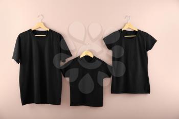 Hangers with blank black t-shirts on color background�