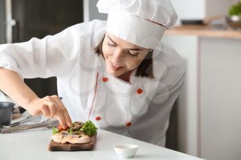 Young female chef preparing tasty dish in kitchen�