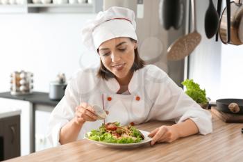 Young female chef preparing tasty salad in kitchen�