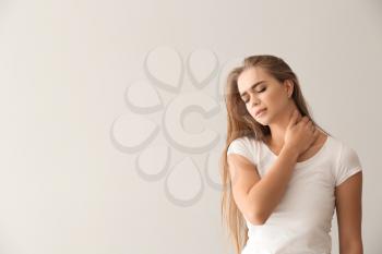 Young woman suffering from neck pain on light background�