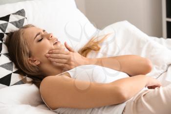 Young woman suffering from toothache while lying in bed�