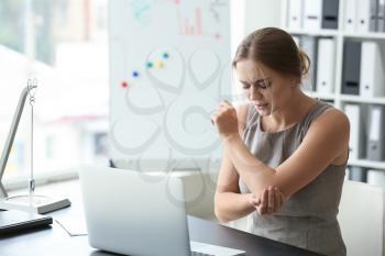 Young woman suffering from pain in elbow at workplace�