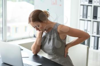 Young woman suffering from back pain in office�