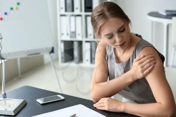Young woman suffering from pain in shoulder at workplace�