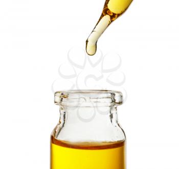 Dripping oil from pipette into glass bottle on white background�
