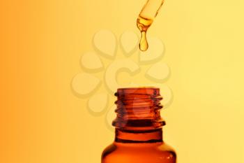 Dripping oil from pipette into glass bottle on color background�