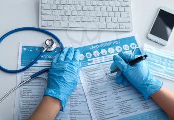 Female doctor filling in laboratory test request form on white table. Health care concept�