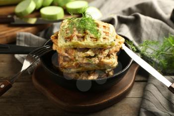 Frying pan with tasty squash waffles on wooden board�