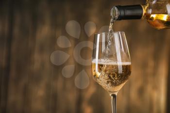 Pouring of white wine from bottle into glass on dark background�