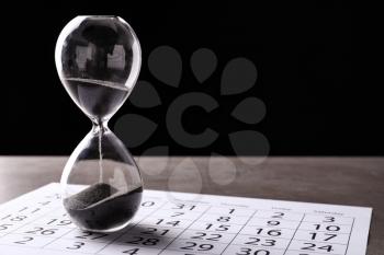 Crystal hourglass with calendar on table. Deadline concept�