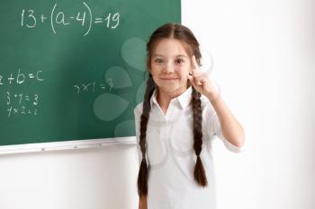 Cute girl standing near chalkboard in classroom�
