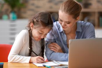 Cute girl with mother doing homework at home�