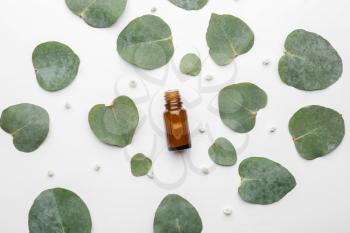 Bottle of eucalyptus essential oil and leaves on white background�