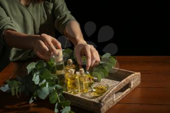 Woman taking bottles of eucalyptus essential oil from tray on table�