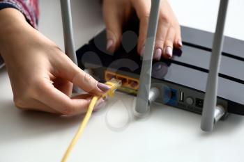 Woman inserting ethernet wire into wi-fi router on white table, closeup�