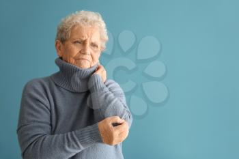 Senior woman suffering from pain in elbow on color background�