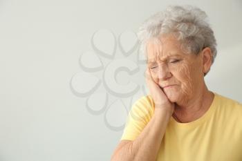 Senior woman suffering from toothache on light background�