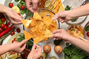 People eating tasty corn chips at white table�