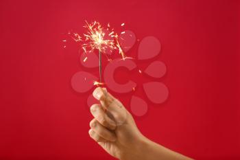 Female hand with Christmas sparkler on color background�