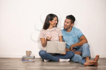 Young couple with laptop sitting on floor near light wall�
