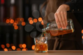 Female bartender pouring whiskey from bottle into glass on table�