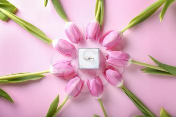 Beautiful engagement ring with tulips on color background, flat lay�