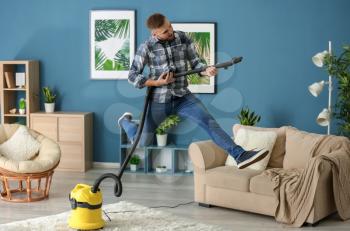 Young man having fun with vacuum cleaner while removing dirt in flat�