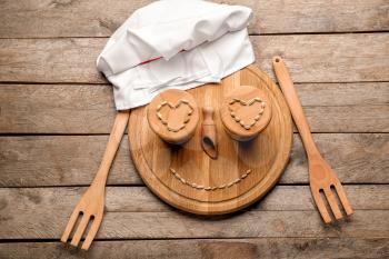 Creative composition with chef's hat, cutting board and kitchen utensils on wooden background�
