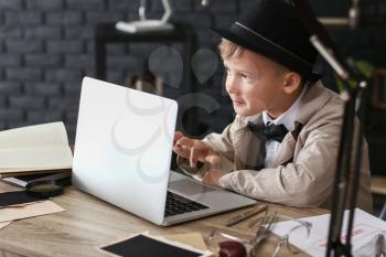 Cute little detective with laptop at table�