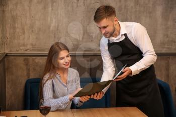 Young waiter showing woman a menu in restaurant�