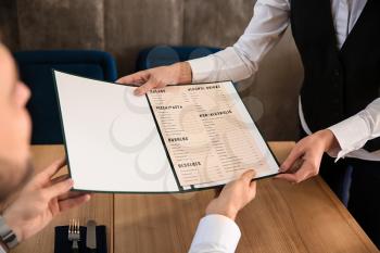 Young waitress showing man a menu in restaurant�