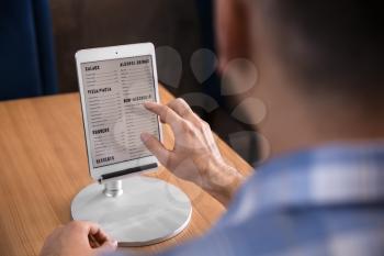 Young man with tablet PC looking through menu in restaurant�