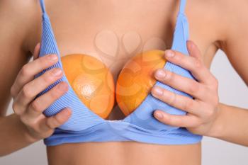 Sexy young woman with grapefruits in her bra on light background, closeup. Erotic concept�