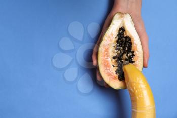 Half of sweet papaya and banana in female hands on color background. Erotic concept�