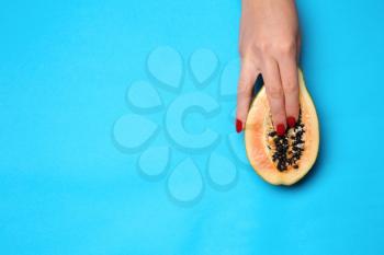 Female hand and half of fresh papaya on color background. Erotic concept�