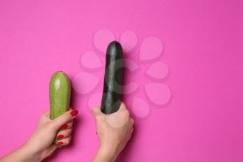 Woman holding two zucchinis on color background. Erotic concept�