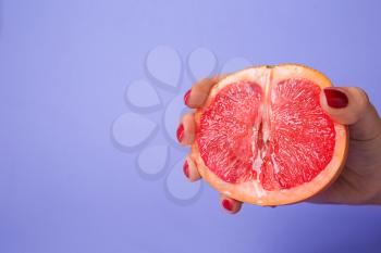 Woman holding half of juicy grapefruit on color background. Erotic concept�