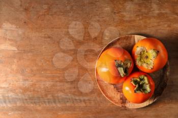 Plate with ripe persimmons on wooden table, top view�