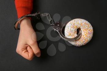 Woman handcuffed to tasty doughnut on dark background. Concept of addiction�