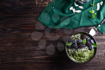 Tasty spirulina smoothie with berries in bowl on dark wooden table�