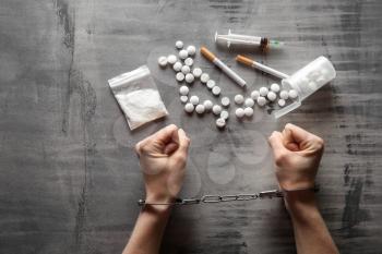 Female junkie in handcuffs with drugs and syringe on grey background. Concept of addiction�