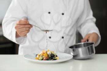 Male chef dressing tasty salad in kitchen, closeup�