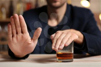 Man with glass of whiskey at table refusing to drink�