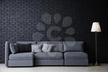 Stylish interior of room with comfortable big sofa near dark brick wall�