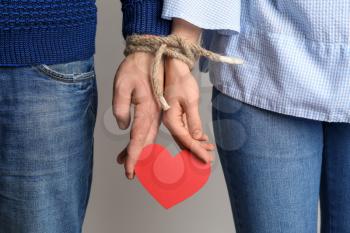 Couple with tied together hands holding paper heart on light background. Concept of addiction�