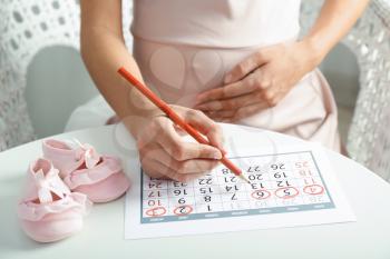 Pregnant woman with calendar sitting at table, closeup�