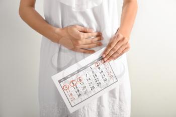Woman with menstrual calendar on light background�