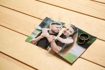 Torn photo of happy couple on wooden background. Concept of divorce�
