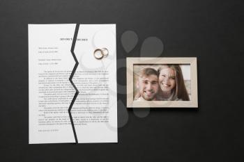 Torn divorce decree, rings and broken frame with photo on dark background�